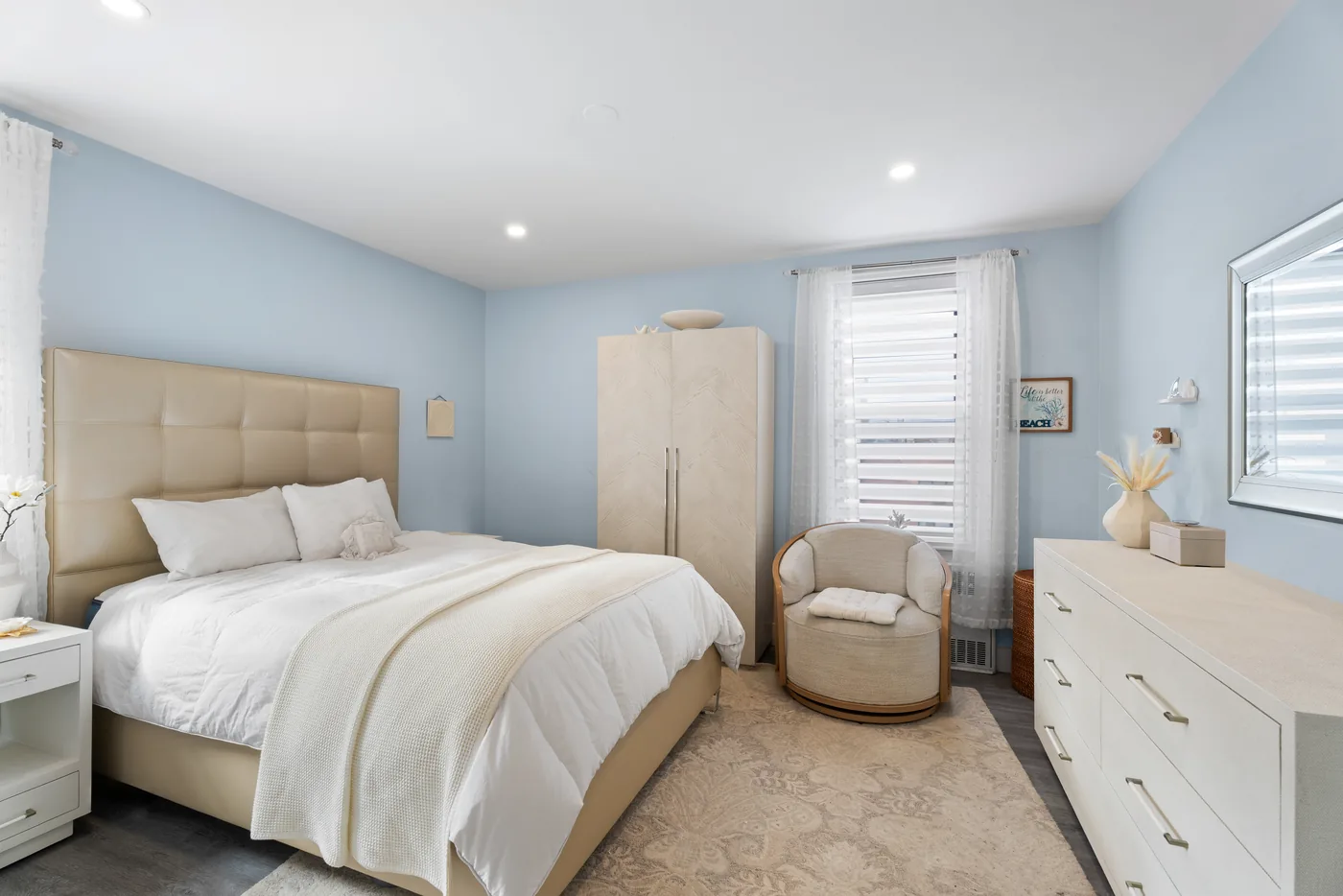Primary bedroom with blue wall and neutral bedding photographed for a New York City real estate listing.